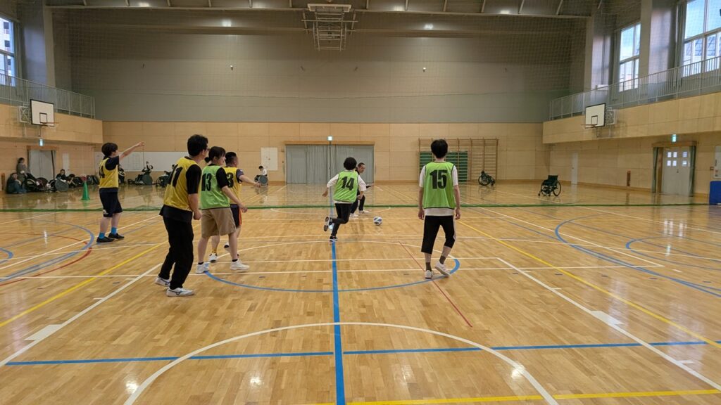 Indoor gym with players in numbered pinnies playing soccer on a polished wooden court, ball in play.